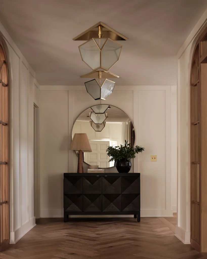 Entryway with black modern console, round mirror, white wall paneling and decorative pendant lighting